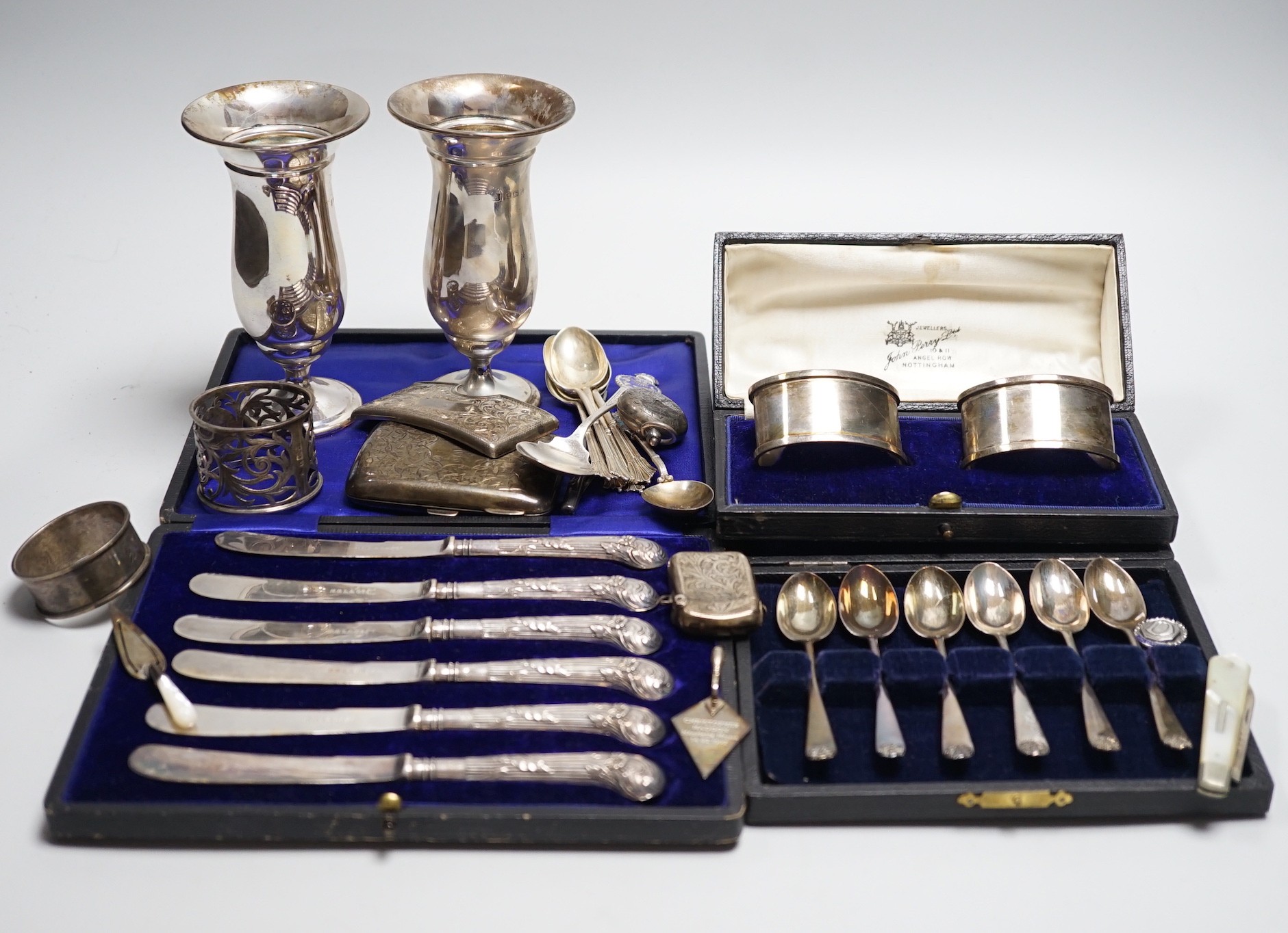 A mixed group of assorted silver ware including a pair of vases, 13.1cm, weighted, cased and loose napkin rings, cased teaspoons, cased silver pistol handled tea knives, sovereign case, mother of pearl handled fruit knif